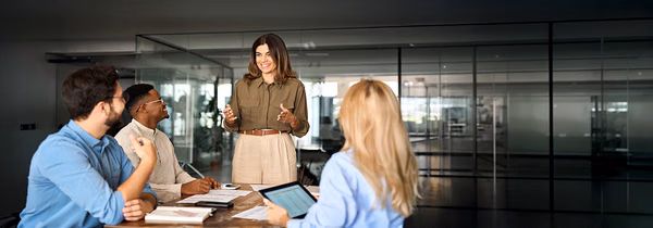 Happy middle aged business woman executive ceo leader discussing project management planning strategy working with diverse colleagues company team at office corporate board group meeting.